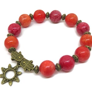 Pu&ograve; includere: Bracciale con perline rosse e arancioni e ciondoli color bronzo. Le perline rotonde sono separate da distanziatori color bronzo. I ciondoli includono un sole e una mano di Hamsa. Un gioiello colorato.