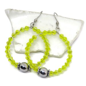 May include: A pair of lime green crystal hoop earrings with silver bead accents. The earrings are made with small, faceted crystals and have a simple, elegant design.