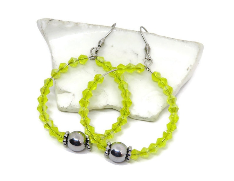 May include: A pair of lime green crystal hoop earrings with silver bead accents. The earrings are made with small, faceted crystals and have a simple, elegant design.