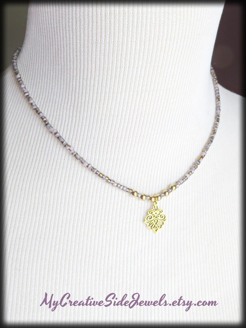 May include: A delicate necklace with a gold-colored pendant in a floral design. The necklace features small, light purple and gold beads. The text "MyCreativeSideJewels.etsy.com" is at the bottom of the image.