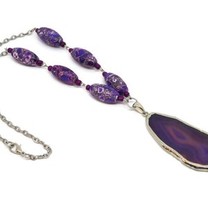 May include: A purple agate pendant necklace with a silver chain and purple and pink patterned beads.