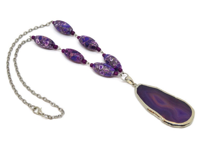 May include: A purple agate pendant necklace with a silver chain and purple and pink patterned beads.