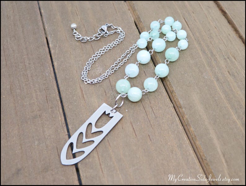 May include: A silver chain necklace with a pendant shaped like a stylised flower. The necklace is strung with light green beads.