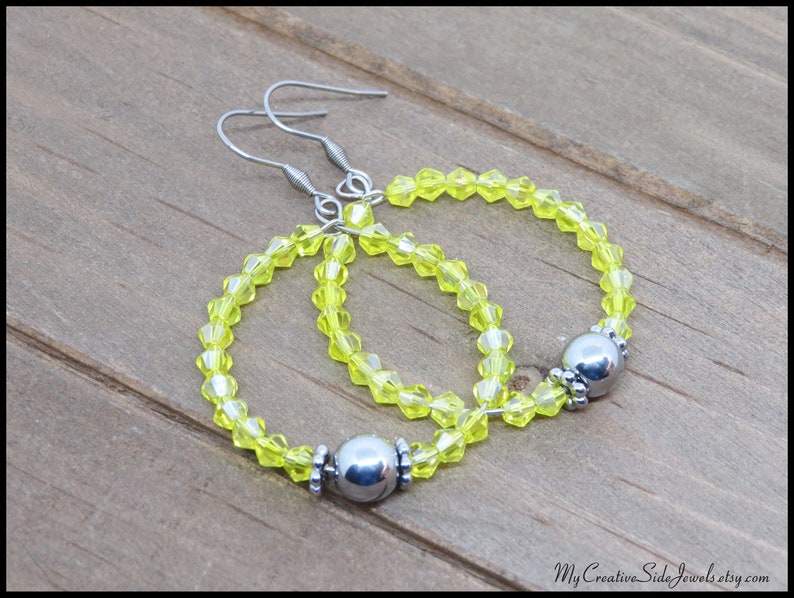 May include: A pair of hoop earrings with silver metal accents and bright yellow beads.