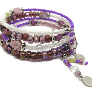 May include: A multi-strand wrap bracelet with purple, white, and burgundy beads. The bracelet features a mix of round and square beads, with dangling charms. The beads are strung on a wire, creating a spiral design.
