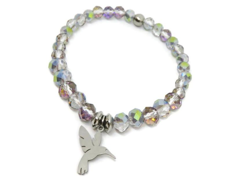 May include: A stretch bracelet composed of faceted, iridescent clear beads with a metallic finish. The bracelet features a silver-toned metal charm shaped like a hummingbird, suspended from a central silver-toned metal bead spacer.