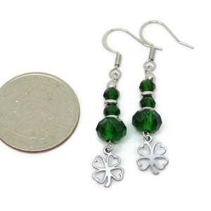 May include: A pair of dangle earrings with green faceted beads and silver-tone clover charms. The earrings have silver-tone ear wires. A U.S. quarter is next to the earrings for size comparison.