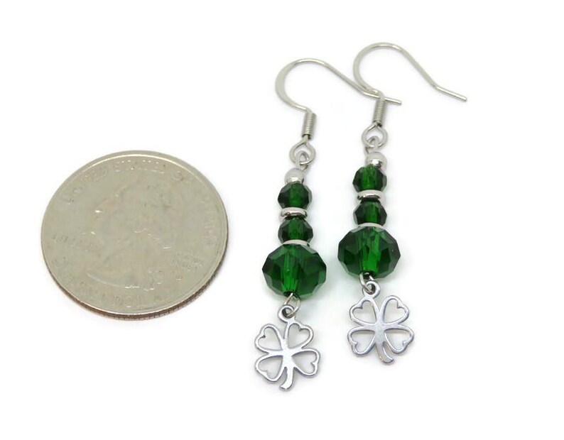 May include: A pair of dangle earrings with green faceted beads and silver-tone clover charms. The earrings have silver-tone ear wires. A U.S. quarter is next to the earrings for size comparison.