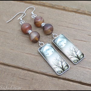 May include: Silver dangle earrings with agate beads and rectangular charms featuring a moon and tree silhouette.