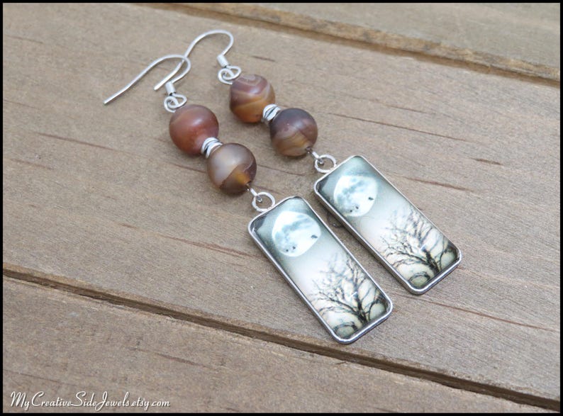 May include: Silver dangle earrings with agate beads and rectangular charms featuring a moon and tree silhouette.