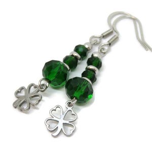 May include: A pair of dangle earrings featuring faceted emerald green beads and silver-tone clover charms. The earrings have silver-tone ear wires and are set against a white background. The earrings are a St. Patrick's Day theme.