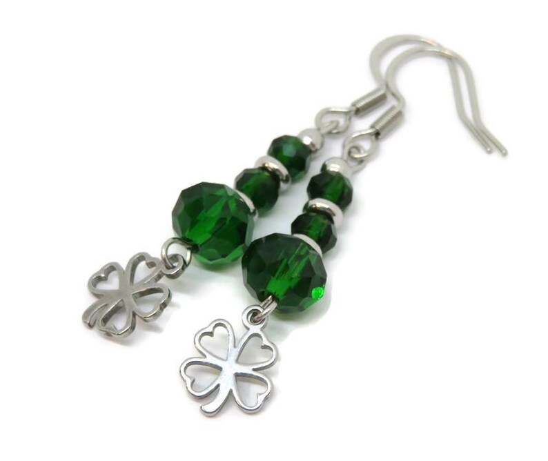 May include: A pair of dangle earrings featuring faceted emerald green beads and silver-tone clover charms. The earrings have silver-tone ear wires and are set against a white background. The earrings are a St. Patrick's Day theme.