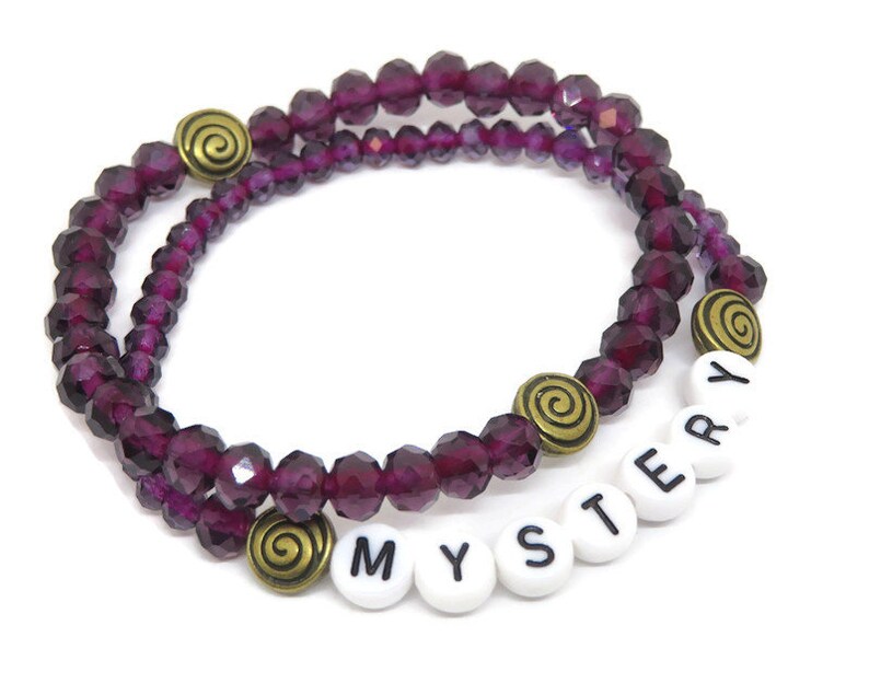 May include: Purple crystal bead bracelet with gold accents and white letter beads spelling "MYSTERY".