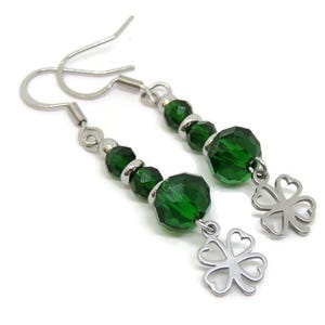 May include: A pair of dangle earrings featuring faceted green beads and silver-tone accents. Each earring has a silver-tone four-leaf clover charm. The earrings are displayed against a white background.