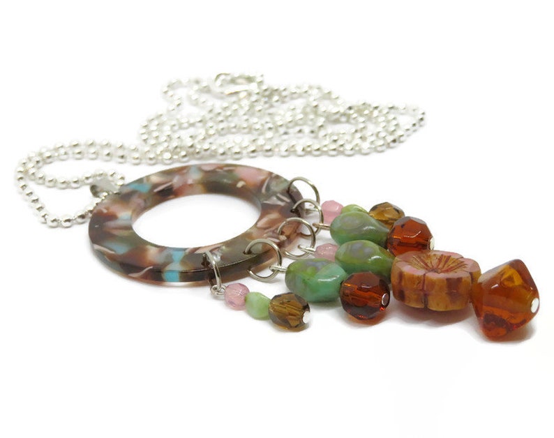 May include: A silver chain necklace with a brown, pink, and blue marbled circle pendant. The pendant has a cluster of colorful glass beads hanging from it, including green, brown, and pink.