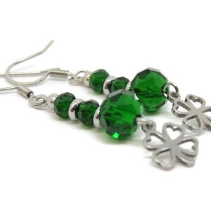 May include: A pair of dangle earrings featuring green faceted beads and silver-tone clover charms. The earrings have silver-tone ear wires and small silver beads between the green beads. The earrings are displayed against a white background.