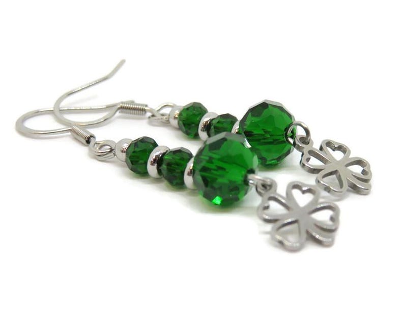 May include: A pair of dangle earrings featuring green faceted beads and silver-tone clover charms. The earrings have silver-tone ear wires and small silver beads between the green beads. The earrings are displayed against a white background.