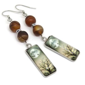 May include: A pair of silver dangle earrings with brown agate beads and rectangular glass charms featuring a moon and tree silhouette.