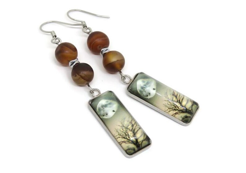 May include: A pair of silver dangle earrings with brown agate beads and rectangular glass charms featuring a moon and tree silhouette.