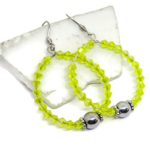 May include: A pair of lime green crystal hoop earrings with silver bead accents. The earrings are made with small faceted crystals and have a simple, elegant design.