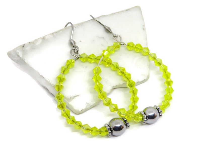 May include: A pair of lime green crystal hoop earrings with silver bead accents. The earrings are made with small faceted crystals and have a simple, elegant design.