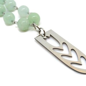 May include: A green jade bead necklace with a silver pendant featuring a cut-out tulip design.