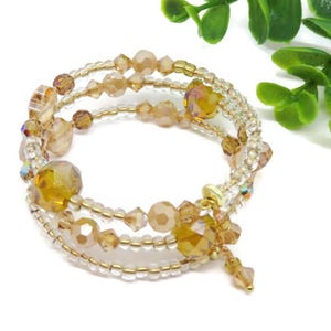 Puede incluir: Pulsera envolvente de m&uacute;ltiples hilos con cuentas claras, doradas y &aacute;mbar. La pulsera en espiral tiene un dije colgante. Las cuentas var&iacute;an en tama&ntilde;o y forma, creando un efecto texturizado y brillante. Una joya elegante.