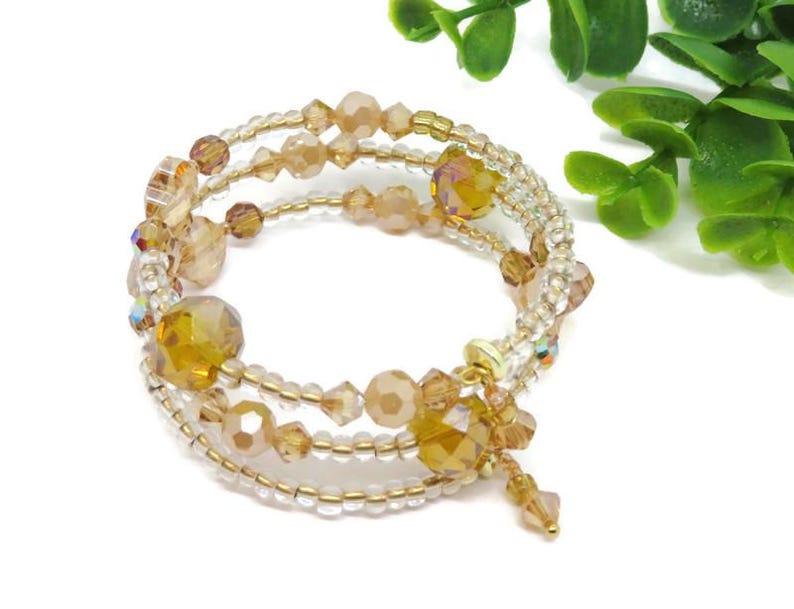 Puede incluir: Pulsera envolvente de m&uacute;ltiples hilos con cuentas claras, doradas y &aacute;mbar. La pulsera en espiral tiene un dije colgante. Las cuentas var&iacute;an en tama&ntilde;o y forma, creando un efecto texturizado y brillante. Una joya elegante.