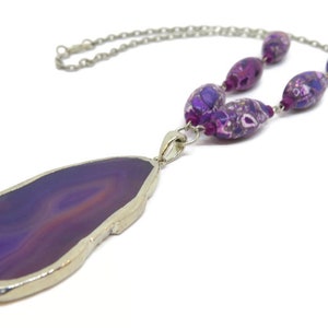 May include: A purple agate pendant necklace with a silver chain and purple and white patterned beads.