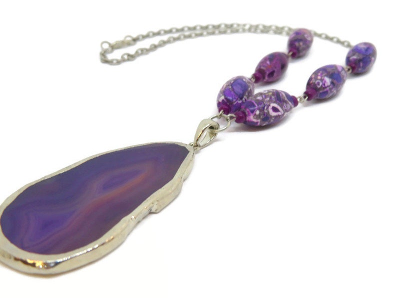 May include: A purple agate pendant necklace with a silver chain and purple and white patterned beads.