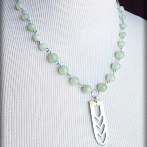 May include: A silver necklace with a pendant shaped like a tulip. The necklace is made with light green beads and a silver chain.