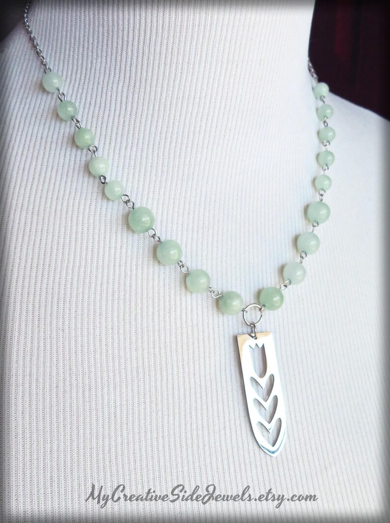 May include: A silver necklace with a pendant shaped like a tulip. The necklace is made with light green beads and a silver chain.