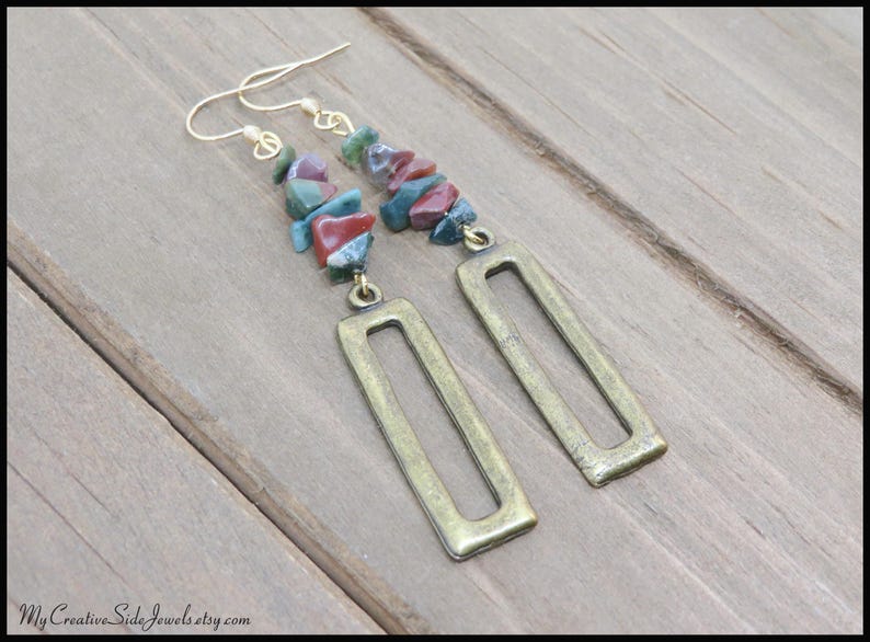 May include: A pair of long, gold-toned earrings with a rectangular pendant. The earrings are adorned with a cascade of colourful, irregularly shaped stones.