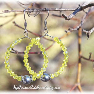 May include: A pair of yellow beaded hoop earrings with silver accents. The earrings are hanging from a branch.