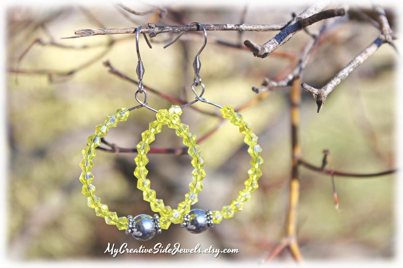 May include: A pair of yellow beaded hoop earrings with silver accents. The earrings are hanging from a branch.