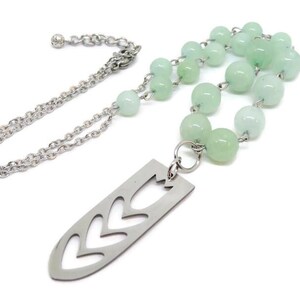 May include: A silver chain necklace with a silver pendant featuring a cut-out design of a leaf. The necklace is adorned with light green beads.