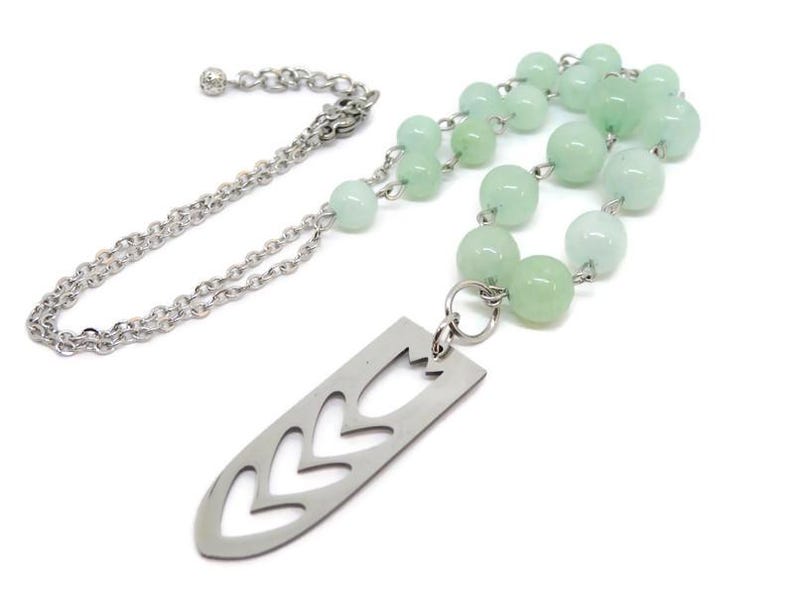 May include: A silver chain necklace with a silver pendant featuring a cut-out design of a leaf. The necklace is adorned with light green beads.