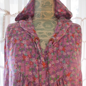 May include: A purple hooded robe with a floral print and wooden toggles. The robe has a gathered neckline and a flowing silhouette.