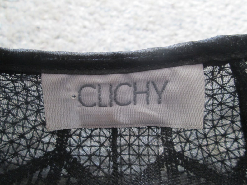 May include: A white tag with black embroidered text that reads "CLICHY" on a black mesh fabric.