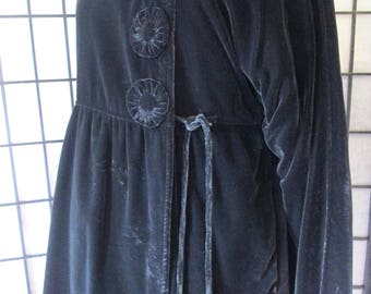May include: A long, black velvet coat with long sleeves and a gathered waist. The coat features three decorative, circular buttons and a matching tie closure. The fabric has a soft, luxurious sheen.