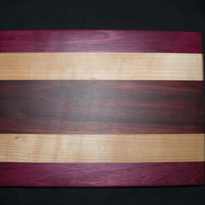 May include: A rectangular wooden chopping board with alternating stripes of purple, light brown, and dark brown wood.