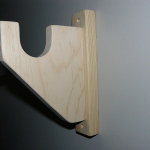 May include: A wooden wall mount with a curved shelf, ideal for displaying items. The mount is made of natural wood with a light brown finish.