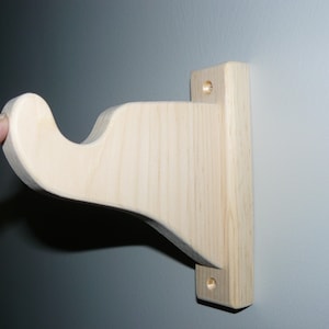 Könnte beinhalten: Eine Holz-Regalhalterung mit einem gebogenen Arm, die zum Stützen von Regalbrettern gedacht ist. Die Halterung ist aus unbehandeltem, hellem Holz gefertigt und hat zwei vorgebohrte Löcher zur Montage.