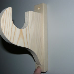 May include: A wooden shelf bracket with a curved design. The bracket is made of unfinished light wood and has a hole drilled in the back for mounting.