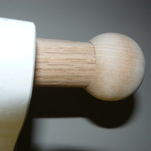 May include: A close-up of a wooden curtain rod finial. The finial is a simple, round shape and is made of light-colored wood.