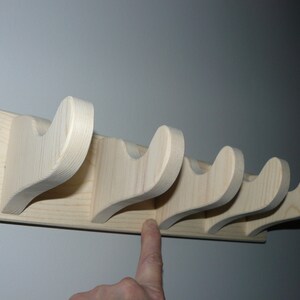 May include: A wooden wall-mounted coat rack with five hooks. The hooks are shaped like a curved line and are made of natural wood.