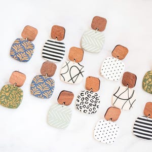 Puede incluir: Un conjunto de 12 pares de pendientes cuadrados colgantes hechos a mano con varios patrones, incluyendo diseños geométricos, florales y de estampados de animales. Los pendientes están hechos de arcilla polimérica y tienen tapas de madera.