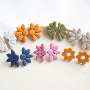 Op de afbeelding: Een set van acht kleurrijke bloemvormige oorbellen. De oorbellen zijn gemaakt van polymer clay en zijn verkrijgbaar in verschillende kleuren, waaronder oranje, groen, wit, blauw en roze.