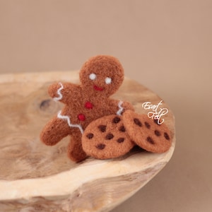 Pu&ograve; includere: Un omino di pan di zenzero con glassa bianca e puntini rossi, e due biscotti al cioccolato con gocce di cioccolato su una superficie di legno.
