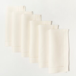 Puede incluir: Seis servilletas de tela color crema dispuestas en diagonal. Cada servilleta doblada presenta un borde decorativo cosido a lo largo de un borde. Las servilletas est&aacute;n hechas de una tela lisa de color s&oacute;lido.